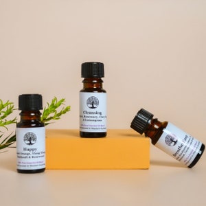 May include: Three small brown glass bottles with black caps containing essential oil blends. The bottles are labelled "Happy", "Cleansing", and "Breathe Easy". Each label features a tree with a circle around it and the text is in purple.