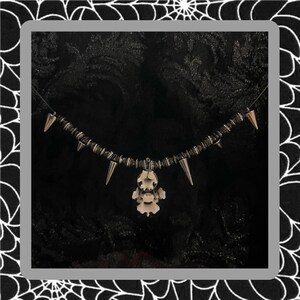 May include: A silver necklace with a black cord and silver spikes. The necklace has a pendant in the shape of a small skeleton.