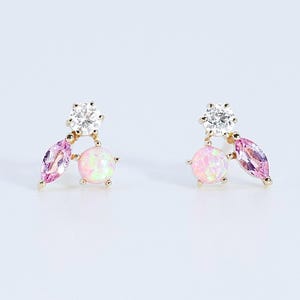 May include: A pair of gold stud earrings, each featuring a cluster of three stones: a clear round-cut stone at the top, a pink marquise-cut stone on one side, and a round iridescent opal-like stone on the other side, all set in gold metal.