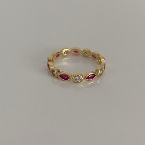 May include: A gold band ring with alternating marquise-shaped pink stones and round white stones.