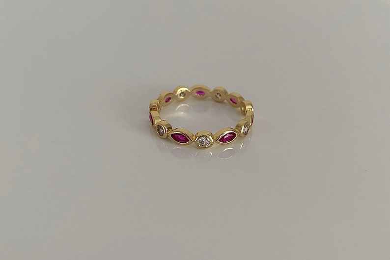 May include: A gold band ring with alternating marquise-shaped pink stones and round white stones.