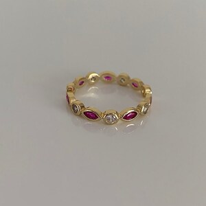 May include: A gold band ring with alternating marquise-shaped pink stones and round white stones.