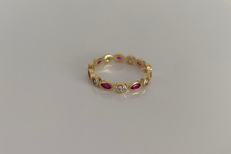 May include: A gold band ring with alternating marquise-shaped pink stones and round white stones.