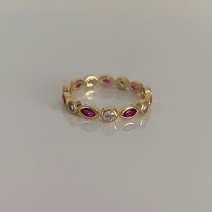 May include: A gold band ring with alternating marquise-shaped pink gemstones and round white gemstones.