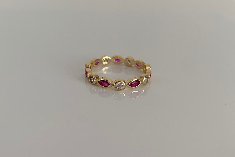 May include: A gold band ring with alternating marquise-shaped pink gemstones and round white gemstones.