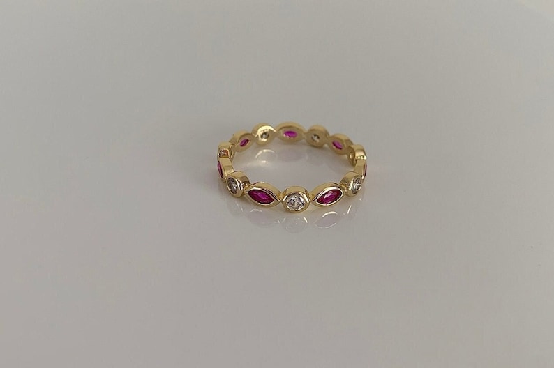 May include: A gold band ring with alternating marquise-shaped pink stones and round white stones.