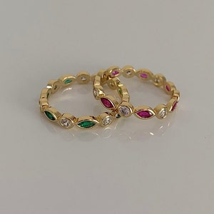 May include: Two gold rings with a row of small, clear, round stones and alternating green and pink marquise-shaped stones.