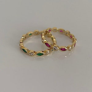 May include: Two gold rings with a row of marquise-shaped stones. One ring has green stones and the other has pink stones.