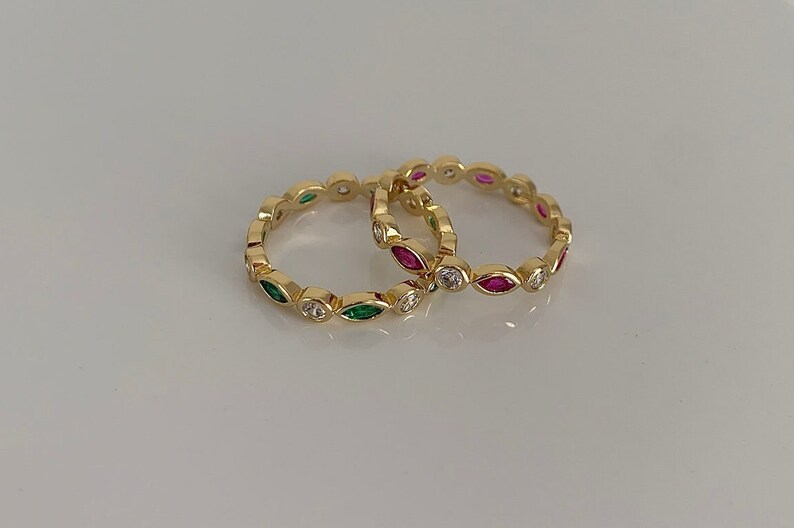 May include: Two gold rings with a row of marquise-shaped stones. One ring has green stones and the other has pink stones.