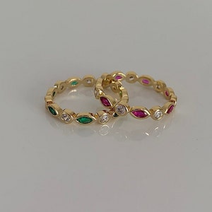 May include: Two gold rings with a row of marquise-shaped stones. One ring has green stones and the other has pink stones.