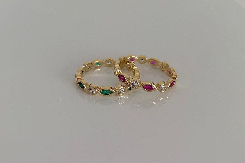 May include: Two gold rings with a row of marquise-shaped stones. One ring has green stones and the other has pink stones.