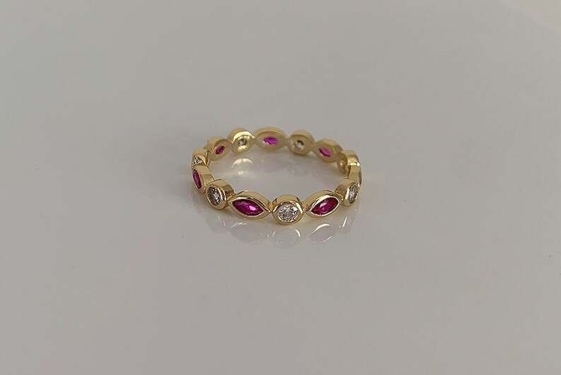 May include: A gold band ring with alternating marquise-shaped pink gemstones and round white gemstones.
