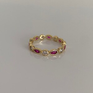 May include: A gold band ring with alternating marquise-shaped pink stones and round white stones.
