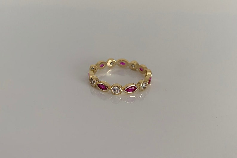 May include: A gold band ring with alternating marquise-shaped pink stones and round white stones.