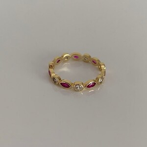 May include: A gold band ring with alternating marquise-shaped red gemstones and round white gemstones.