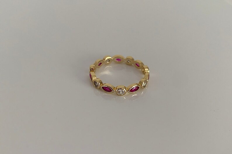 May include: A gold band ring with alternating marquise-shaped red gemstones and round white gemstones.