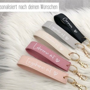 Könnte beinhalten: Fünf Schlüsselanhänger mit verschiedenen farbigen Lederbändern und goldenen Schlüsselringen. Die Bänder sind mit dem Text "Corinna", "Lehrerin mit", "Lehrerin mit", "Erzieherin mit" und "Lehrerin mit" in weißer Schrift personalisiert. Jedes Band hat ein kleines weißes Herz.