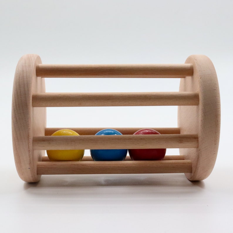 K&ouml;nnte beinhalten: Ein Holzspielzeug mit drei bunten B&auml;llen im Inneren. Die B&auml;lle sind gelb, blau und rot. Das Spielzeug ist aus Naturholz gefertigt und f&uuml;r Babys und Kleinkinder konzipiert.