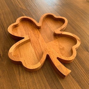 May include: A wooden four-leaf clover shaped serving dish. The dish is made of light brown wood and has a natural finish.
