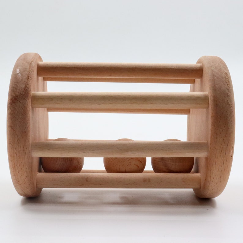 K&ouml;nnte beinhalten: Ein Holzspielzeug mit drei Holzkugeln, die in einem zylindrischen K&auml;fig rollen. Das Spielzeug ist aus Naturholz gefertigt und hat eine glatte Oberfl&auml;che.