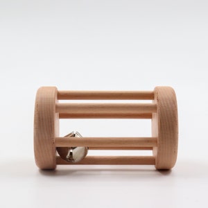 K&ouml;nnte beinhalten: Ein Holzspielzeug mit einer Glocke im Inneren. Das Spielzeug ist aus Naturholz gefertigt und hat eine zylindrische Form mit einer Reihe horizontaler St&auml;be.