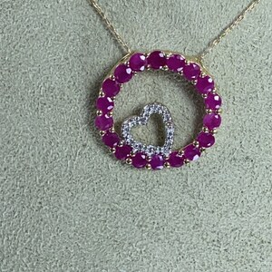 May include: A gold necklace with a pendant featuring a circle of pink gemstones surrounding a smaller heart-shaped pendant with smaller white gemstones.