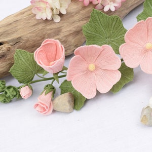 May include: A crocheted flower arrangement featuring pink flowers with green leaves and buds. The flowers are arranged on a light brown wooden surface with a white background. The text "LYCHETTE - CROCHET NATURE -" is visible at the bottom of the image.