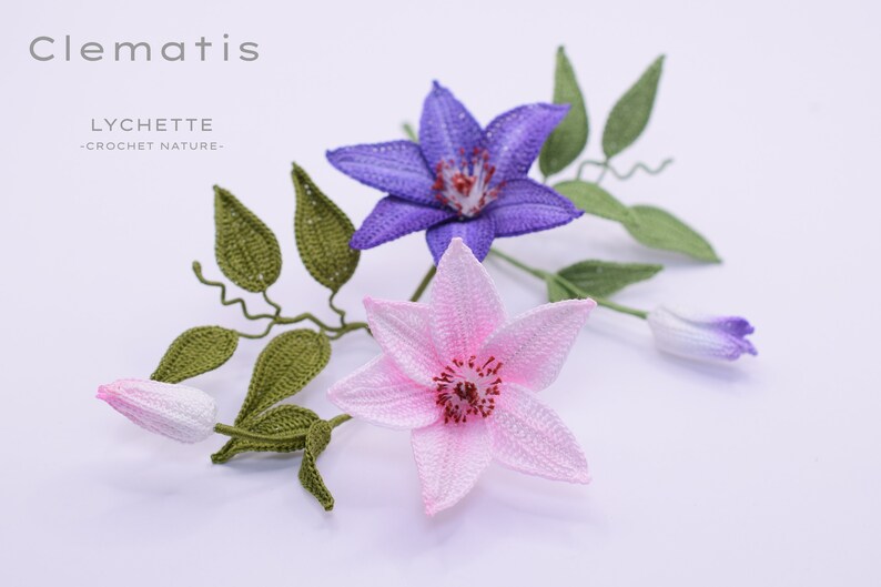 Puede incluir: Primer plano de tres flores de clem&aacute;tide de ganchillo, una morada, una rosa y un capullo. Las flores est&aacute;n en un tallo de ganchillo verde con hojas.