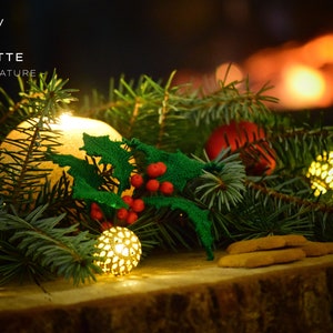 May include: A crocheted holly sprig with red berries, surrounded by evergreen branches and small, glowing, golden lights. The text "Holly" and "LYCHETTE - CROCHET NATURE" is visible in the image.
