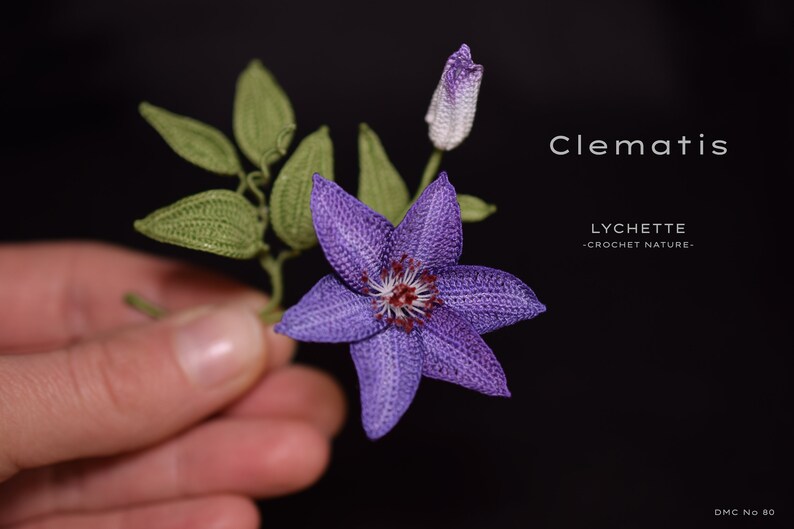 Puede incluir: Una flor de clem&aacute;tide de color p&uacute;rpura hecha a crochet con hojas verdes y un capullo. La flor se sostiene en una mano. El texto "Clematis" y "LYCHETTE - CROCHET NATURE." es visible en la imagen.