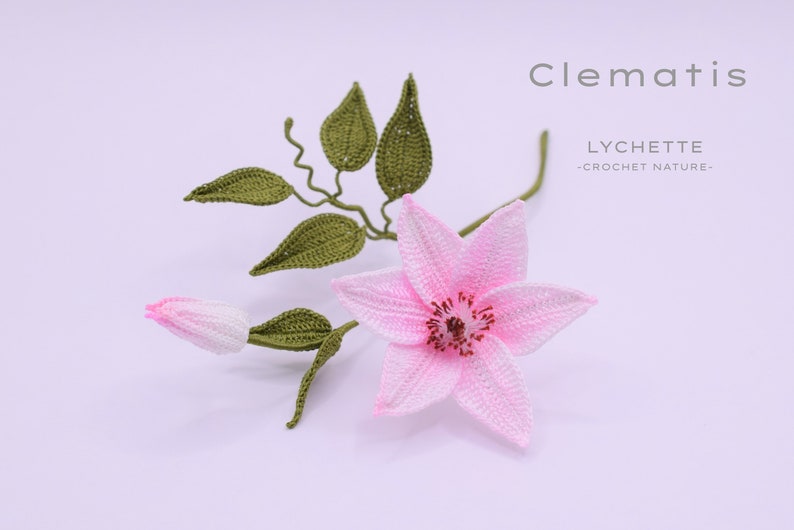 Puede incluir: Una flor de clematis rosa hecha a crochet con hojas verdes. La flor es delicada e intrincada, con un centro detallado. Las hojas tambi&eacute;n est&aacute;n hechas a crochet y tienen una textura realista. La flor est&aacute; etiquetada como "Clematis" y "LYCHETTE -CROCHET NATURE-."