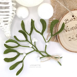 Op de afbeelding: Een groene gehaakte misteltak met witte kralen, een ronde houten hanger met de tekst "Boże Narodzenie 24.12.20" en een jute achtergrond.
