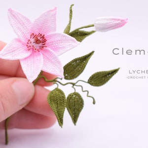 Puede incluir: Una flor de clematis rosa hecha a crochet con hojas verdes y un capullo. La flor se sostiene en una mano. El texto "Clematis" y "LYCHETTE -CROCHET NATURE- " es visible en la imagen.