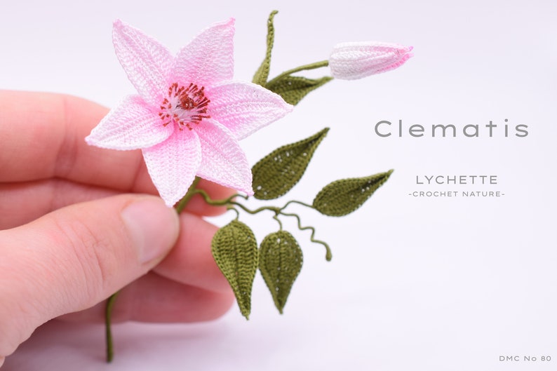 Puede incluir: Una flor de clematis rosa hecha a crochet con hojas verdes y un capullo. La flor se sostiene en una mano. El texto "Clematis" y "LYCHETTE -CROCHET NATURE- " es visible en la imagen.