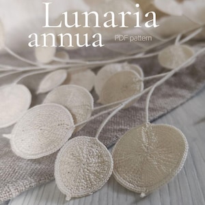 Puede incluir: Primer plano de un patrón de ganchillo con el texto "Lunaria annua PDF pattern". La imagen presenta hojas y tallos de ganchillo blanquecinos, con un fondo de tonos neutros. La palabra "LYCHETTE" está en la parte inferior.