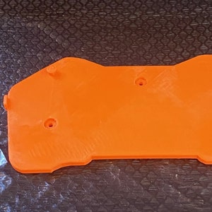 May include: Orange plastic 3D printed part with five screw holes. A small bag of screws is next to the part.