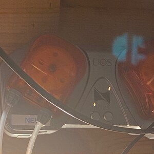 May include: A close-up of a gray and white device with two clear orange pumps. The device has the word "DOS" printed on it. The pumps are connected to clear tubing.