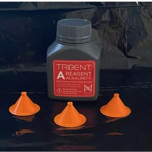 Peut inclure: Une bouteille grise étiquetée "Trident A Réactif Alcalinité" avec trois entonnoirs en plastique orange. La bouteille porte une étiquette d'avertissement et des instructions pour se connecter au tube de prélèvement rouge.