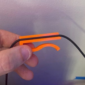May include: Orange plastic cable management clip holding a black cable.