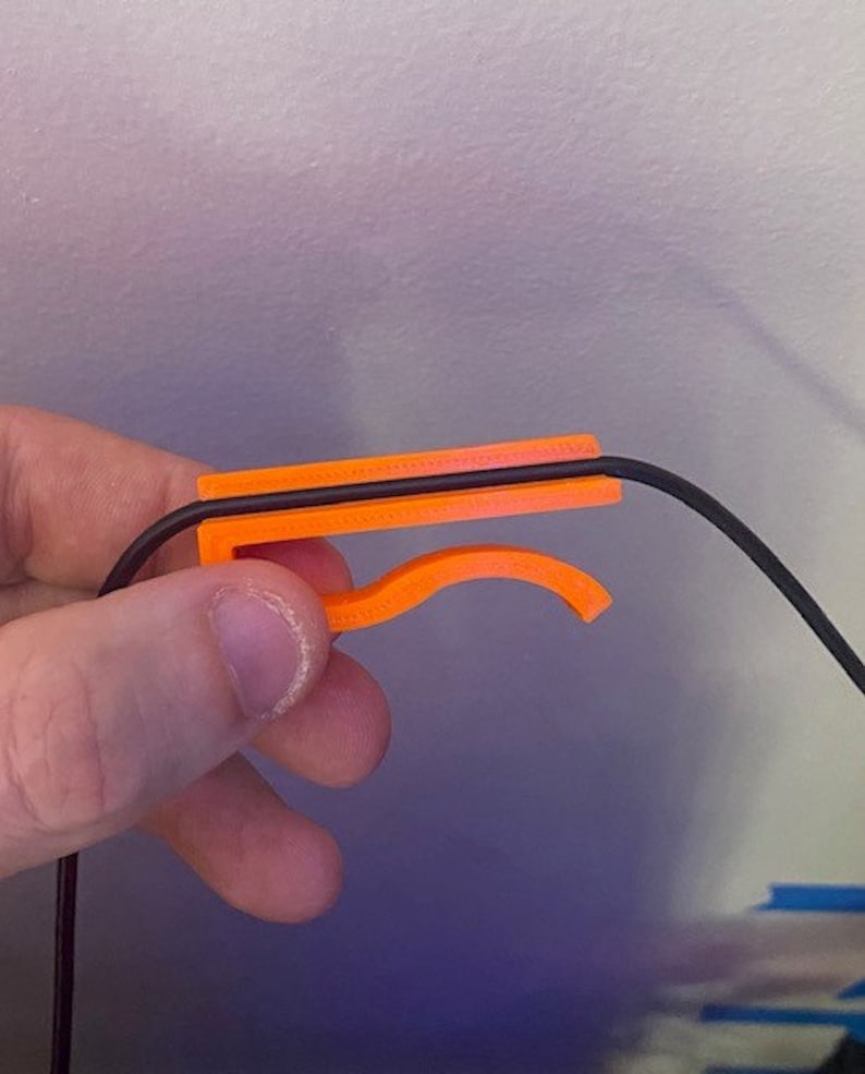 May include: Orange plastic cable management clip holding a black cable.