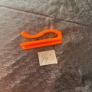 May include: Orange plastic clip measuring 1/4 inch. The clip is shaped like a curved line with a flat base.
