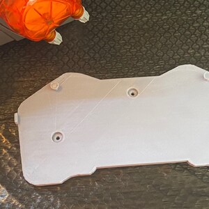 May include: A white plastic 3D printed mounting plate with four screw holes. The plate has a rounded, irregular shape.