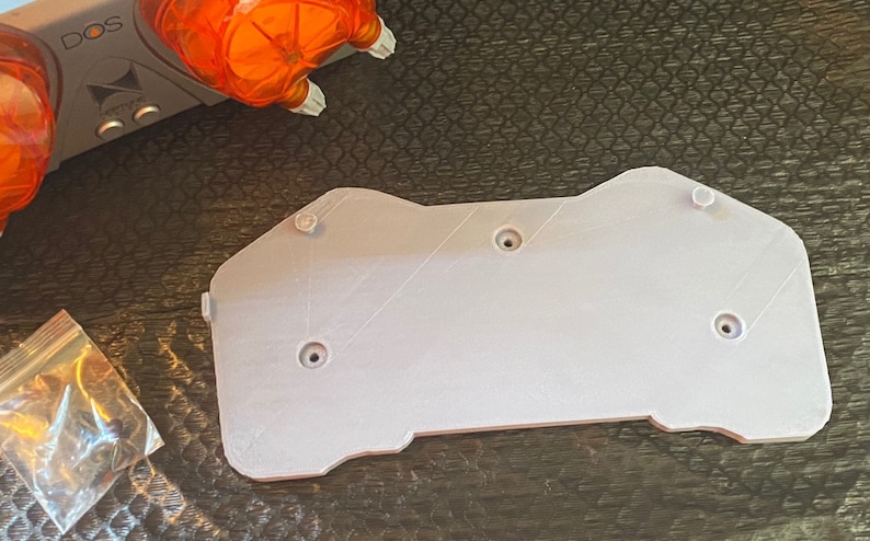 May include: A white plastic 3D printed mounting plate with four screw holes. The plate has a rounded, irregular shape.