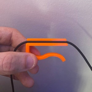 May include: An orange plastic cable organizer with a curved hook. The cable organizer is designed to hold a single cable in place.