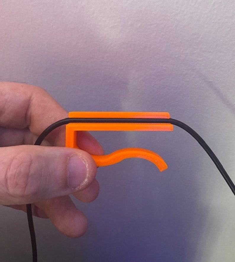 May include: An orange plastic cable organizer with a curved hook. The cable organizer is designed to hold a single cable in place.