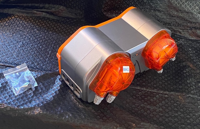 May include: A silver and orange dual-channel dosing pump with two clear orange dosing heads. The pump has a label that says "DOS" and one of the dosing heads has a label that says "MAG".