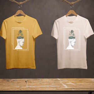 Puede incluir: Dos camisetas con un dise&ntilde;o gr&aacute;fico de una persona con un bosque creciendo de su cabeza. El texto en las camisetas dice "Soy naturaleza". Una camiseta es amarilla y la otra es blanca.