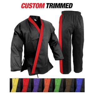 May include: Black martial arts uniform with red trim on the jacket and pants. The words "CUSTOM TRIMMED" are in red at the top. A row of colored belts is at the bottom, including yellow, red, purple, orange, green, and brown.