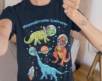May include: A navy blue t-shirt with a graphic of dinosaurs in space wearing astronaut helmets. The text "Neurodiverse Universe" is printed on the shirt.