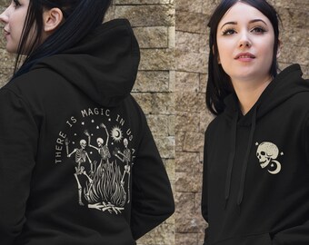 May include: Black hoodie with a front pocket and a hood. The back of the hoodie features a graphic of dancing skeletons around a bonfire with the text "THERE IS MAGIC IN US ALL". The front has a skull with stars and a crescent moon.
